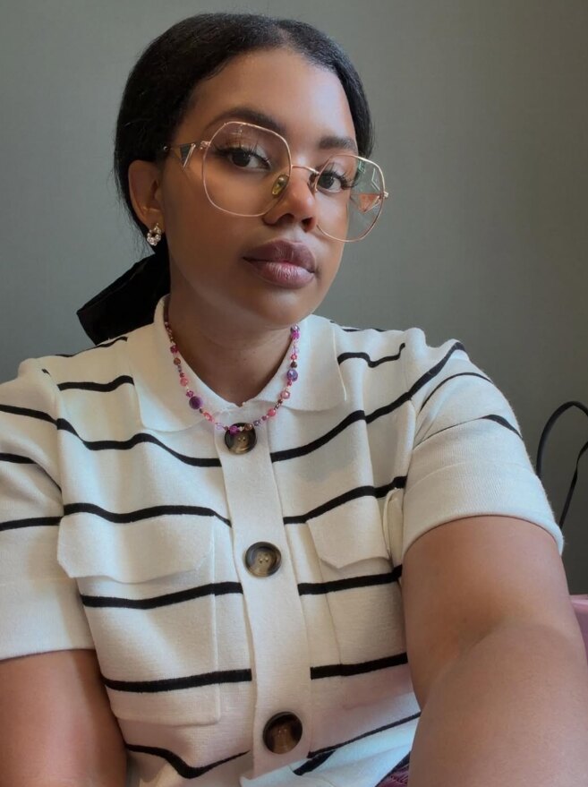 The owner of A.Kai Adornments, wearing round gold glasses and a beaded pink necklace