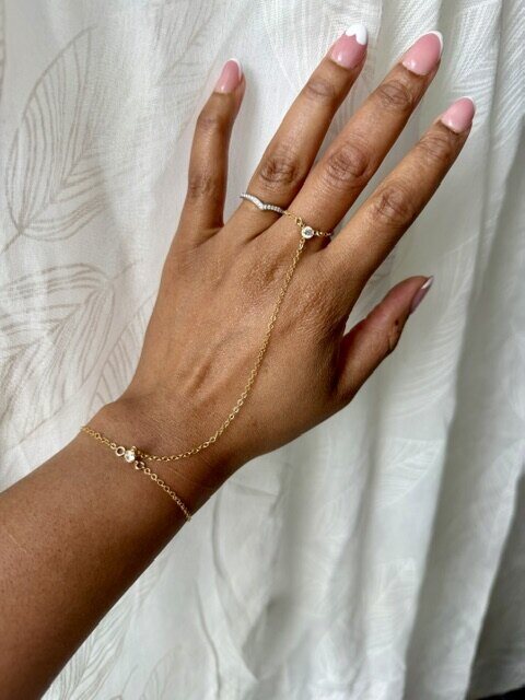 A gold hand chain with a small stone ring and bracelet