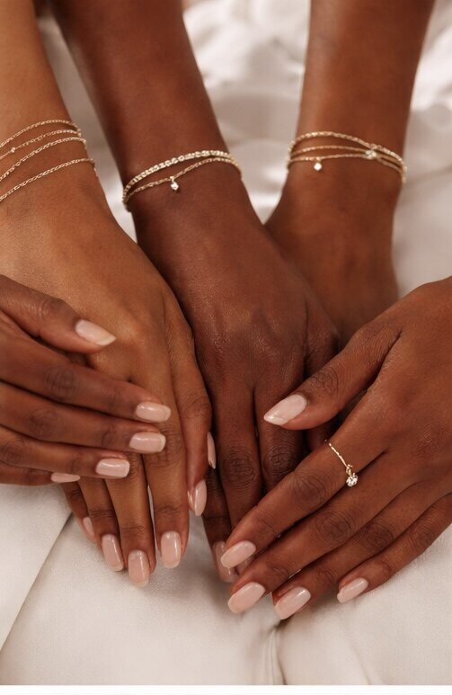 Three sets of hands wearing delicate gold bracelets and a ring